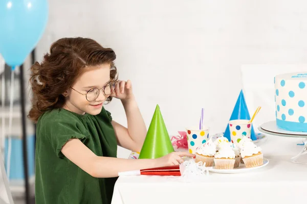 Adorable kid sitting at table with cupcakes during birthday celebration — Stock Photo