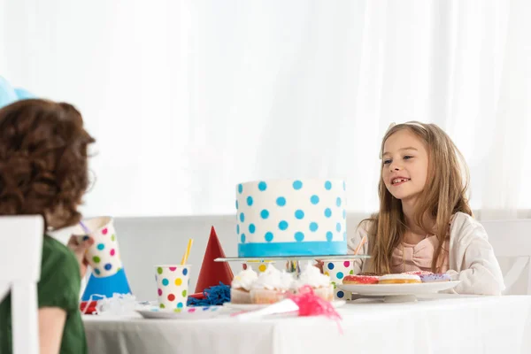 Adorables niños sentados en la mesa de la fiesta con pastel durante la celebración del cumpleaños - foto de stock