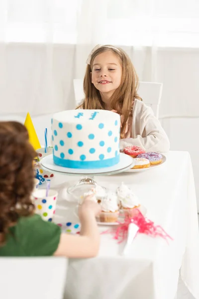 Adorable kids sitting at party table with cake during birthday celebration — Stock Photo