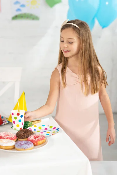 Adorable kid at birthday table with festive decorations and donuts during party — Stock Photo