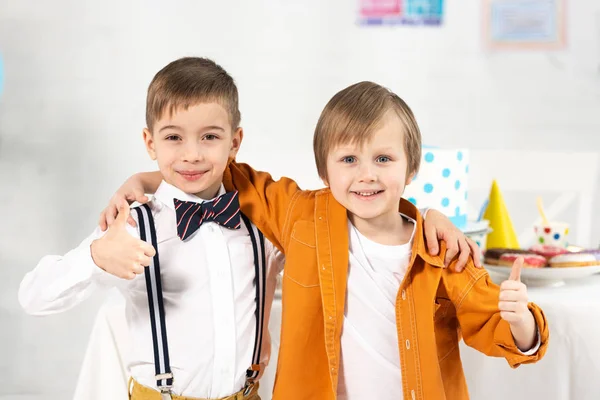 Adorable preteen garçons regardant caméra, câlins et montrant pouces pendant fête d'anniversaire — Photo de stock