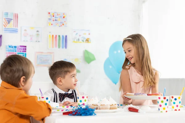 Criança sorrindo segurando prato com donuts durante festa de aniversário com amigos em casa — Fotografia de Stock