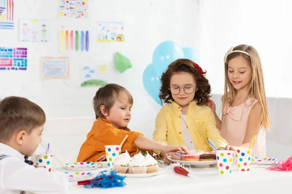 Crianças adoráveis sentadas na mesa de festa com bolo durante a celebração de aniversário em casa — Fotografia de Stock