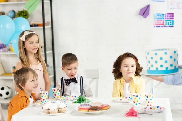 Прелестные дети сидят за столом и ждут торт во время празднования дня рождения — стоковое фото