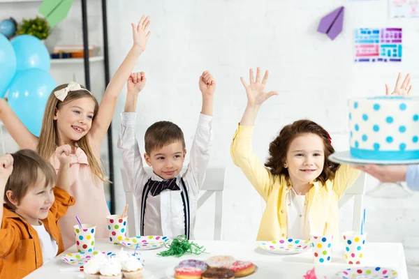 Прелестные дети сидят за столом, аплодируют и ждут торт во время празднования дня рождения — стоковое фото