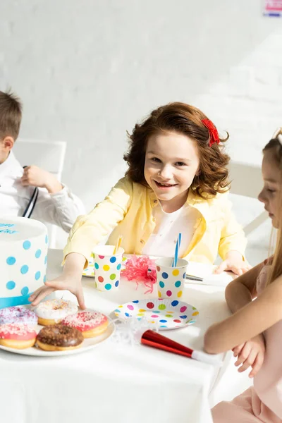 Adorables niños sentados en la mesa con rosquillas durante la fiesta de cumpleaños en casa — Stock Photo