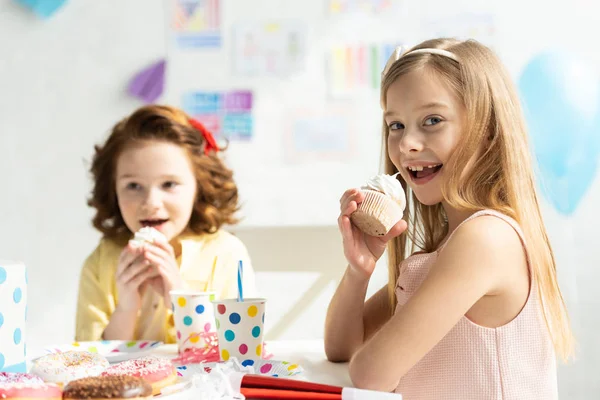 Adorables enfants assis à la table de fête et mangeant des cupcakes pendant la célébration d'anniversaire — Photo de stock