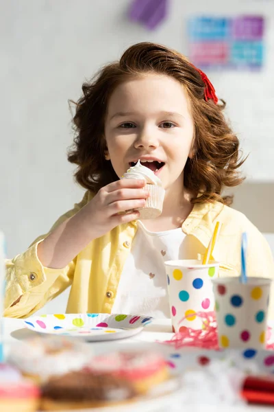 Adorable preadolescente comer magdalena y mirando a la cámara mientras celebra cumpleaños en casa - foto de stock