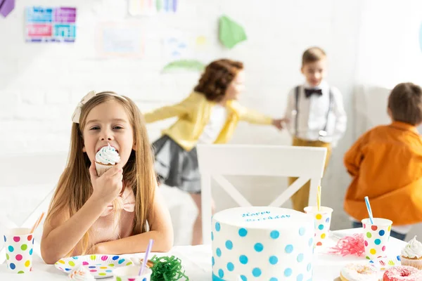 Selective focus of adorable kid sitting at table and eating cupcake during birthday party — Stock Photo