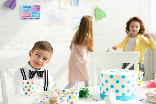 Selective focus of adorable boy looking at camera and sitting at party table during birthday celebration — Stock Photo