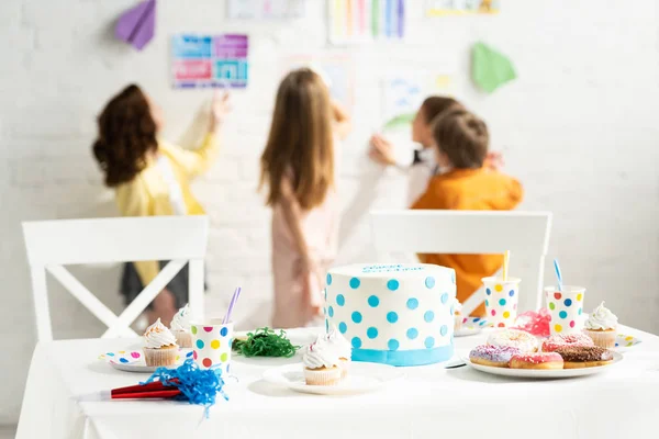 Selective focus of table with birthday cake, party horns, paper cups, cupcakes and donuts — Stock Photo
