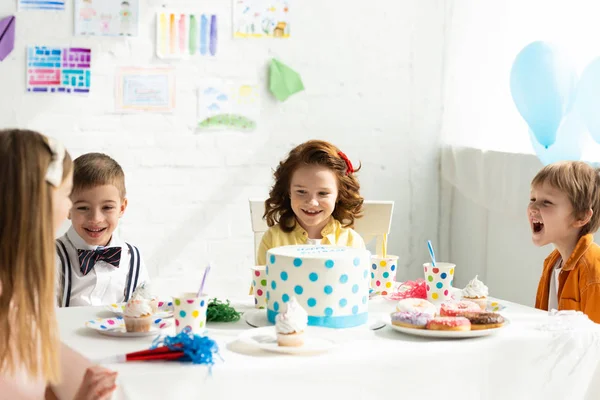 Очаровательные улыбающиеся дети сидят за столом и веселятся во время празднования дня рождения — стоковое фото