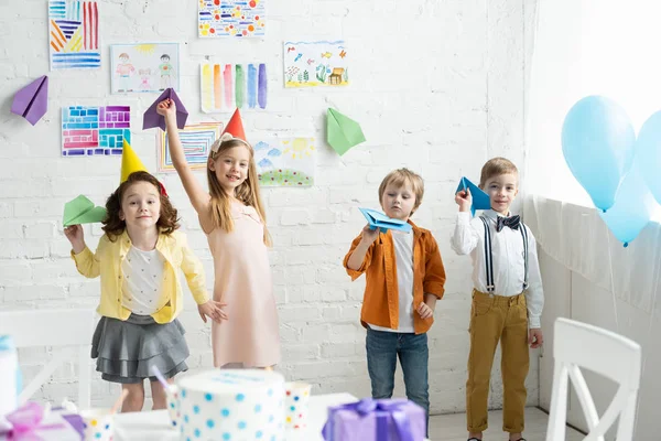 Очаровательные улыбающиеся дети играют с бумажными самолетами во время празднования дня рождения дома — стоковое фото