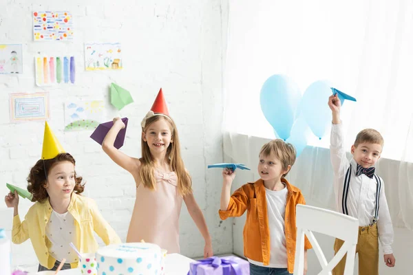 Adorables niños sonrientes jugando con aviones de papel durante la fiesta de cumpleaños en casa - foto de stock