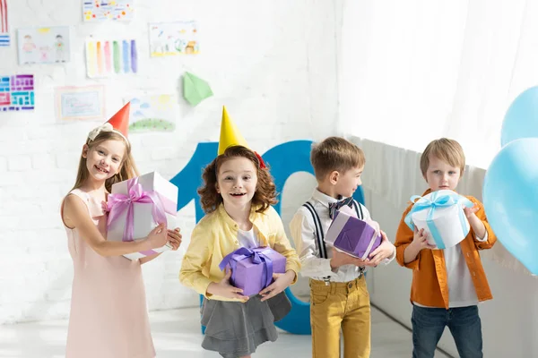 Entzückend lächelnde Kinder mit Geschenken und Blick in die Kamera bei der Geburtstagsparty zu Hause — Stockfoto