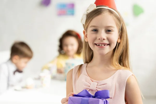 Adorable happy kid holding present and looking at camera during birthday celebration — Stock Photo