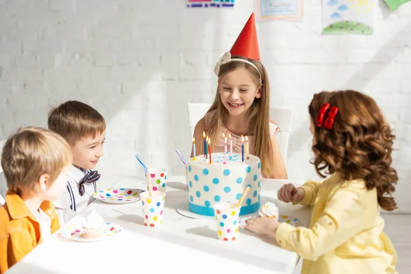 Adorable happy kids sitting at party table with cake while celebrating birthday together — Stock Photo