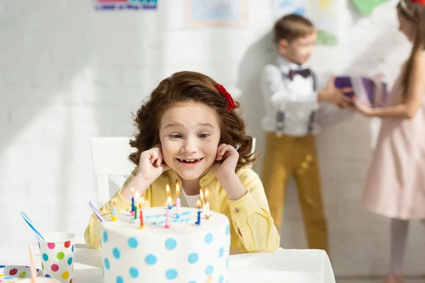 Selective focus of adorable happy kid at table looking at birthday cake during party — Stock Photo