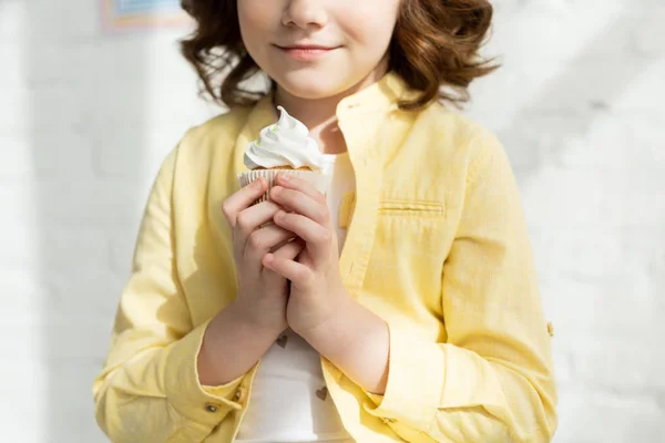 Vista ritagliata del bambino in giallo che tiene deliziosi cupcake a casa — Foto stock