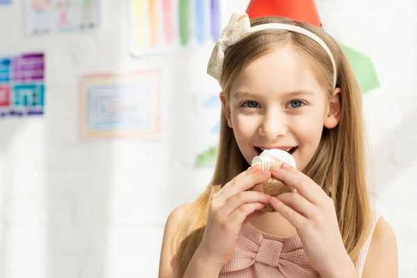 Entzückende Preteen in Stirnband Cupcake essen und in die Kamera schauen — Stockfoto