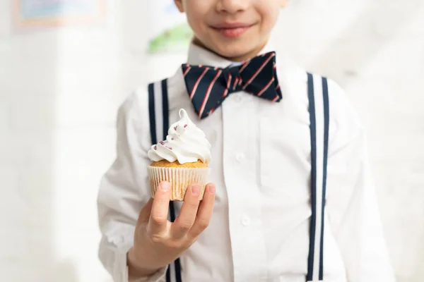 Vista cortada de menino pré-adolescente em gravata arco segurando delicioso cupcake — Fotografia de Stock