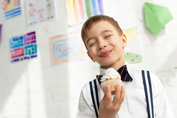 Adorable preteen boy in bow tie holding cupcake and smiling with eyes closed — Stock Photo