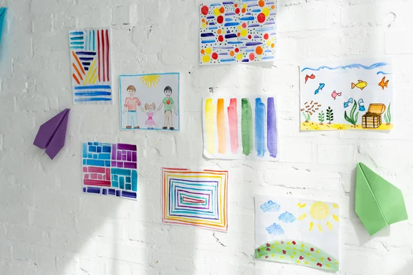 Peintures colorées pour enfants et avions en papier sur mur de briques blanches — Photo de stock