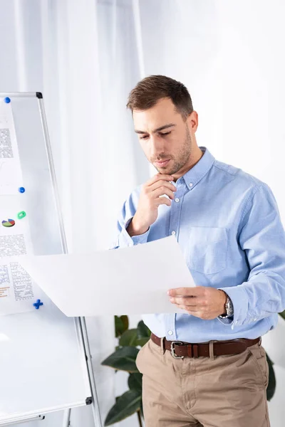 Nachdenklicher Geschäftsmann schaut auf leeres Papier, während er im Büro neben Whiteboard steht — Stockfoto