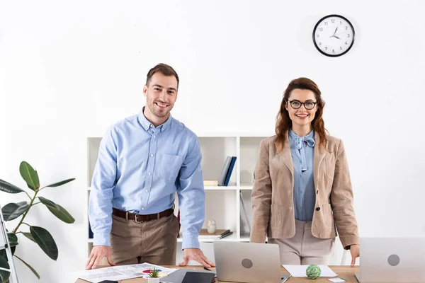 Mujer alegre en gafas de pie con hombre de negocios en la oficina - foto de stock