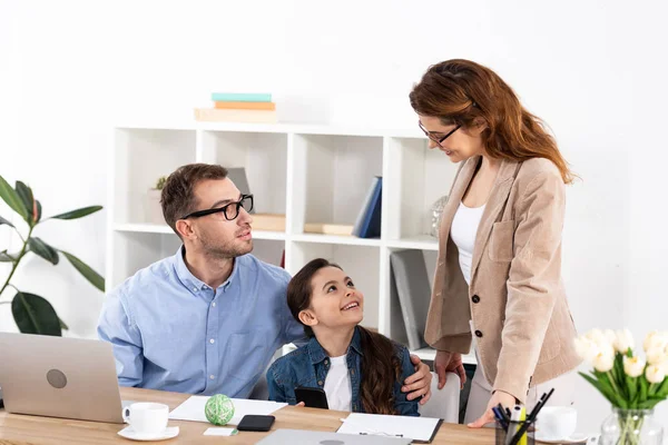 Cheerful kid sitting with father and looking at mother in glasses — Stock Photo