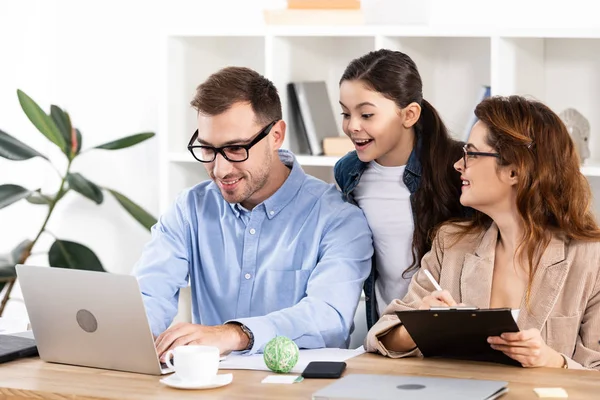 Cheerful kid looking at laptop near father and mother in glasses — Stock Photo
