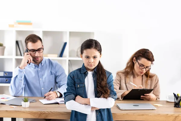 Selective focus of upset kid with crossed arms near parents in office — Stock Photo
