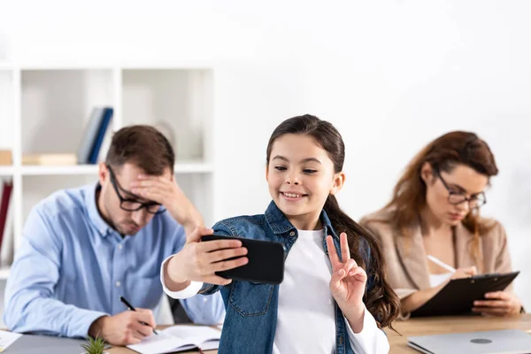 Selective focus of happy child taking selfie on smartphone near parents in glasses — Stock Photo