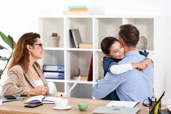 Cheerful kid hugging father near mother in office — Stock Photo