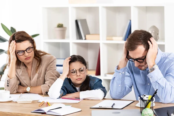 Lindo niño en gafas sentado con padres exhaustos en la oficina - foto de stock