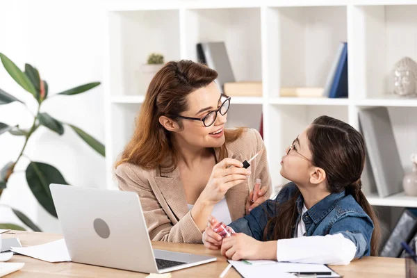 Mère gaie appliquant gloss lèvre sur fille mignonne au bureau — Photo de stock