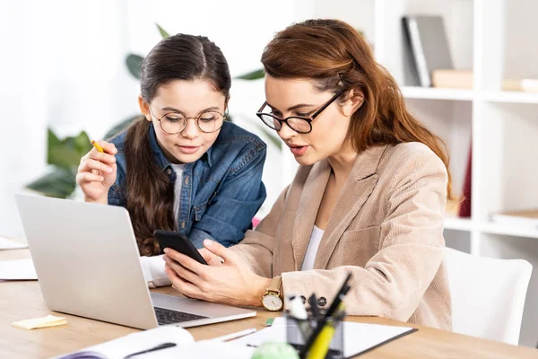 Cute kid looking at smartphone near attractive mother in glasses — Stock Photo