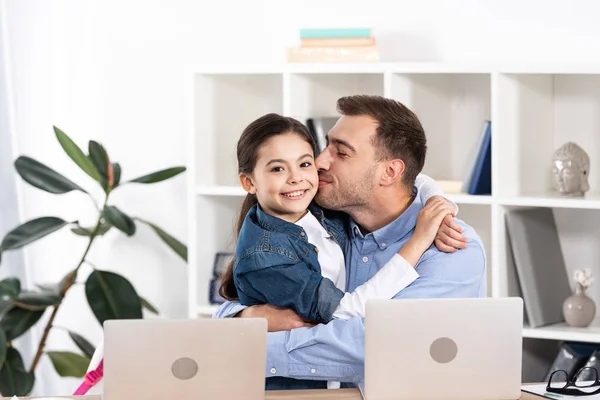 Feliz padre besos mejilla de alegre hija en oficina - foto de stock