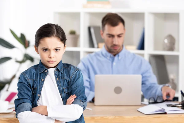 Selective focus of upset kid standing with crossed arms near father in office — Stock Photo