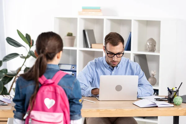 Selective focus of father in glasses using laptop near daughter in office — Stock Photo