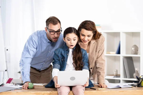 Удивленные родители смотрят на ноутбук рядом с дочерью в офисе — стоковое фото