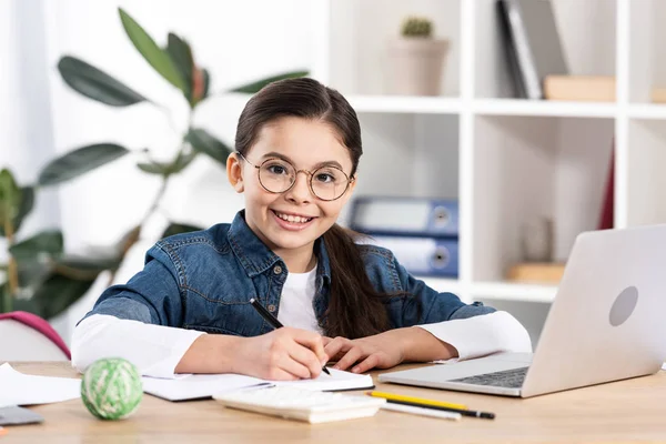 Glückliches nettes Kind schaut in die Kamera in der Nähe von Laptop im Büro — Stockfoto