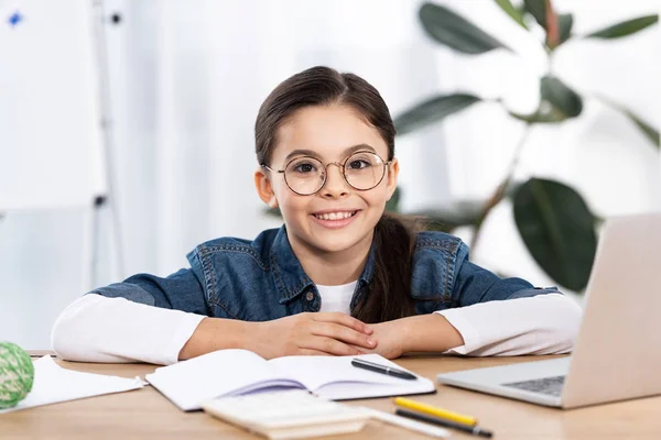 Alegre lindo niño mirando la cámara cerca del ordenador portátil en la oficina — Stock Photo