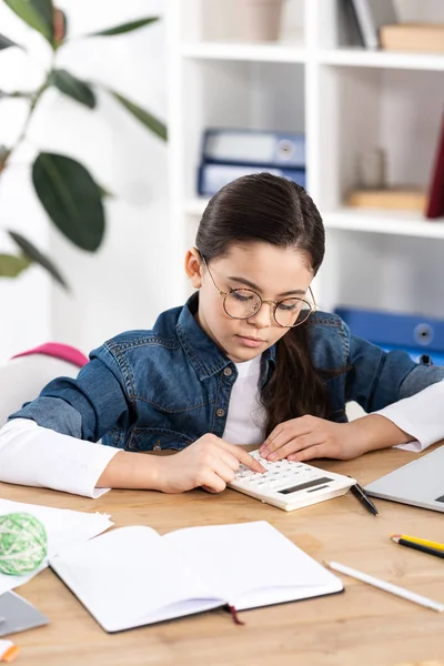 Criança bonito em óculos usando calculadora enquanto sentado no escritório — Fotografia de Stock