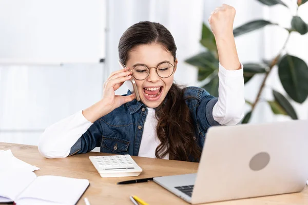 Happy kid celebrating triumph while talking on smartphone in office — Stock Photo