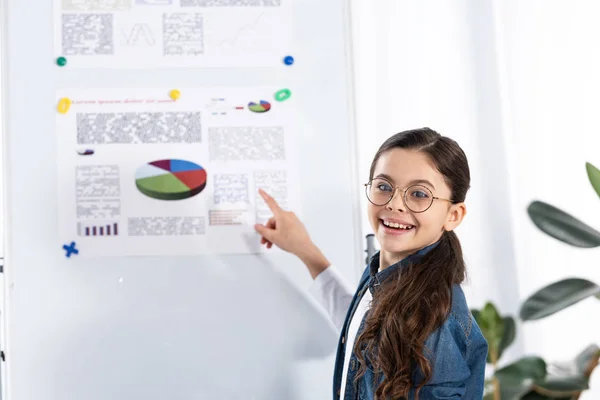 Happy kid in glasses pointing with finger at white board with charts and graphs — Stock Photo