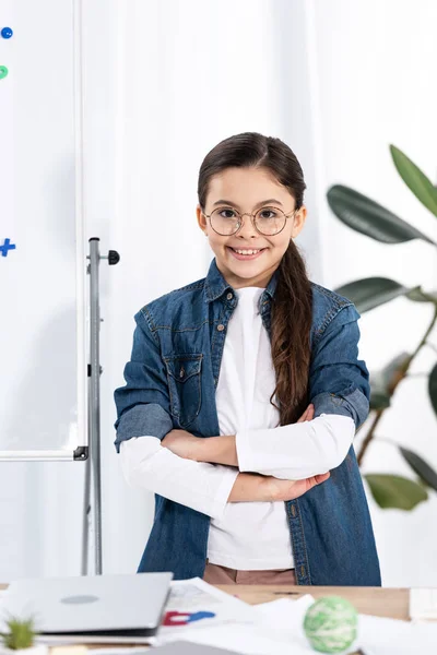 Весела дитина, що стоїть з схрещеними руками біля білої дошки в офісі — стокове фото