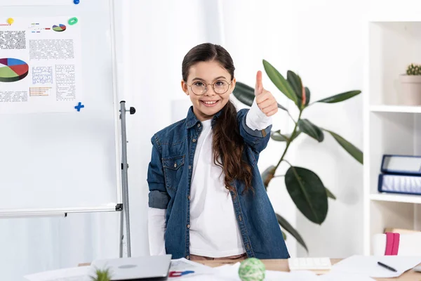 Cheerful kid showing thumb up near white board with charts and graphs — Stock Photo