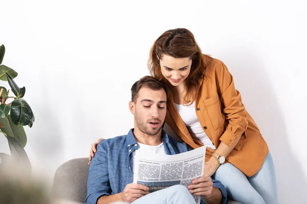 Cheerful woman hugging man and reading newspaper at home — Stock Photo