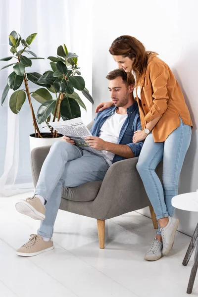 Alegre mujer abrazando guapo hombre con periódico en casa - foto de stock